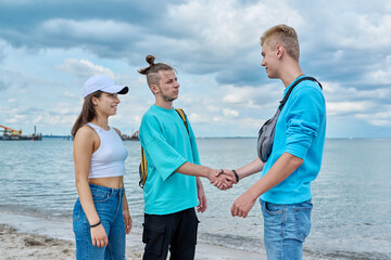 Young teenage friends guys and girl meeting, greeting, shake hands on beach