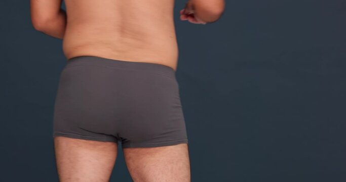Back, buttocks in underwear and a dance for health with a man in studio on a gray background. Beauty, freedom and a model moving in underpants for natural skincare or body positive freedom closeup