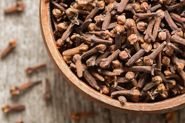 Dry cloves in wooden bowl on rustic table, fresh herb spice concept 