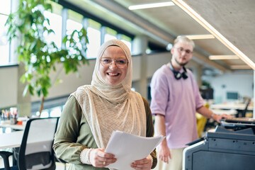 In a modern startup office, a business-minded Muslim woman wearing a hijab collaborates with her colleague, symbolizing diversity, empowerment, and success in the contemporary corporate world