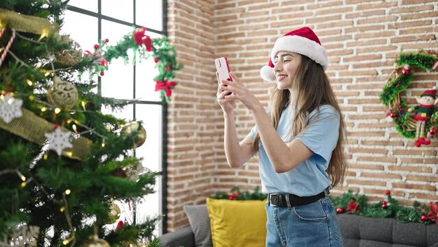 Young beautiful hispanic woman taking photo to christmas tree by smartphone at home