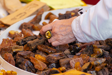 Hand of a woman with a ring choosing amber among many rough pieces of amber of different colours in a street market
