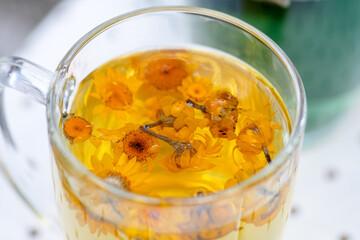 Glass cup with hot water and marigold or calendula flowers for a herbal tea infusion, close up