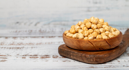 Roasted hazelnuts in wood bowl. Peeled hazelnuts kernel on white wood background. Copy space. Empty space for text