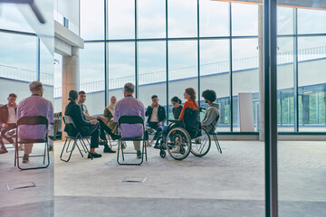 A diverse group of young business entrepreneurs gathered in a circle for a meeting, discussing corporate challenges and innovative solutions within the modern confines of a large corporation