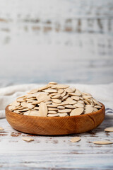 Pumpkin seeds in wooden bowl. Shelled pumpkin seeds on a white wood background