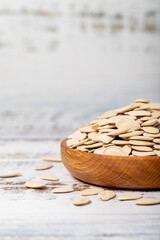 Pumpkin seeds in wooden bowl. Shelled pumpkin seeds on a white wood background. Close up