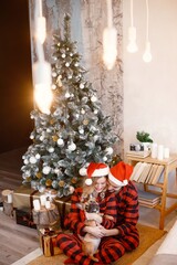 Couple wearing christmas plaid red pajamas sitting on the floor with a dog