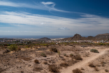 Hiking trail in a desert with a view of a city, sea or ocean and mountains