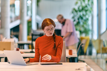 In a modern startup office, a professional businesswoman with orange hair sitting at her laptop, epitomizing innovation and productivity in her contemporary workspace.