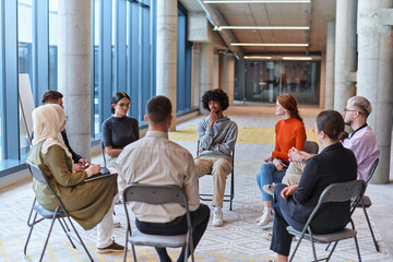 A diverse group of young business entrepreneurs gathered in a circle for a meeting, discussing...