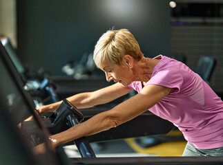 gym sport fitness exercising training mature senior elderly woman running cardio treadmill tired...