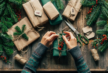 The hands of an unrecognizable woman wrap Christmas gifts on the table in a creative workshop.