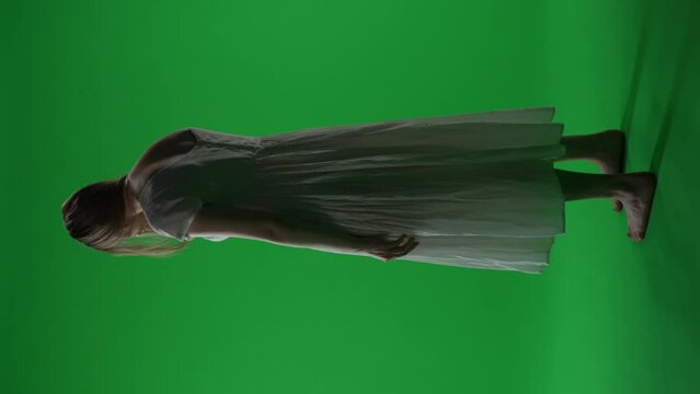 Full-size vertical green screen, chroma key video of a posessed female, woman figure, ghost, poltergeist, zombie turning her face to the camera with a dead look. Chroma key.
