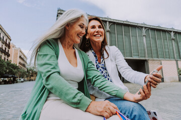 Beautiful senior women meeting outdoors in the city - Two mature female adults friends bonding and having fun while shopping outdoors