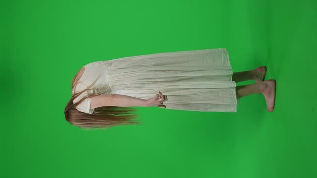 Full-size vertical green screen, chroma key video of a posessed female, woman figure, ghost, poltergeist, zombie turning her face to the camera, abrupt and convulsive. Chroma key.