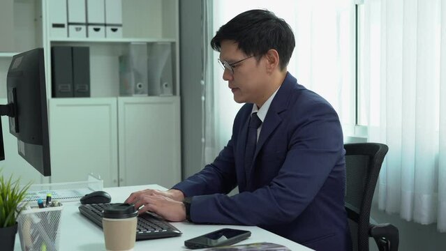 happy asian business man in suit using computer on desk looking at wrist watch check time working to break out office