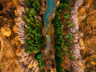 Aerial view of blue river flow through autumn colorful forest.