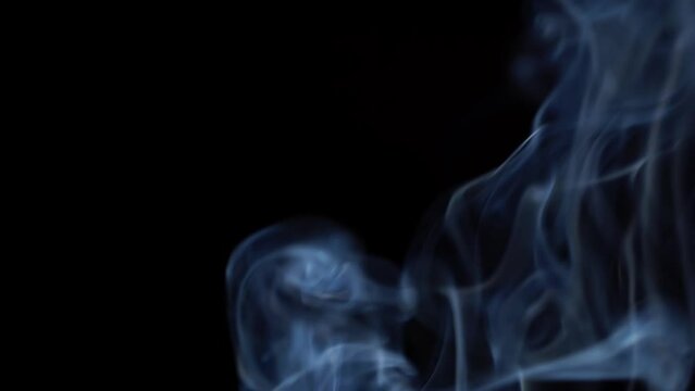 Blue smoke billows on dark background, slow motion