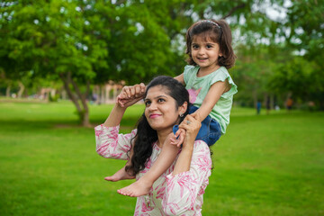 Happy young indian mother carrying child daughter on her shoulders at summer park.Family and...