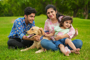 Naklejka na ściany i meble Happy young indian family having fun together at summer park. Mother, father and daughter with labrador dog in garden.