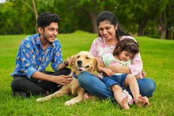 Happy young indian family having fun together at summer park. Mother, father and daughter with labrador dog in garden.