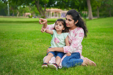 Naklejka na ściany i meble Happy playful young indian mother and cute little girl daughter sitting at summer park or garden.