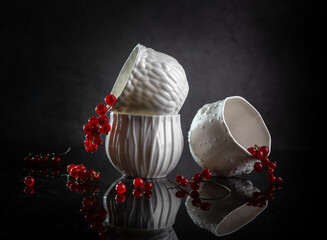 Porcelain white cups with red currants on a dark background