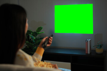 Woman sitting on sofa and watching green screen projector TV, movies on the wall at home