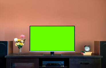 Modern LCD flat-screen TV on a black wooden table with cut green screen in the living room with an amplifier and speaker cabinet at home.