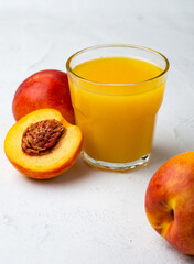 A glass with peach juice, next to it is a cutaway peach on a white background, close up.