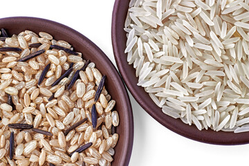 Two clay bowls of white basmati rice and coarse brown black rice. Top view with copy space
