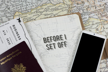 Travel journal open to the 'BEFORE I SET OFF' page, with a passport, boarding pass, and smartphone against a vintage map. Travel documents and tech essentials