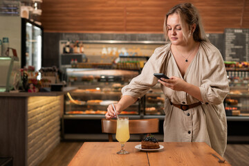 Cute girl food travel blogger hold phone take food photo on phone mobile camera at cafe table