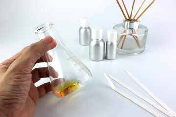 chemical beaker or flask is in left hand , on table with blotting paper , fragrance bottle and...