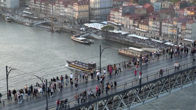 Establishing shot of Porto, Portugal, showing people crossing the Dom Luis I Bridge over the Douro River at sunset.
