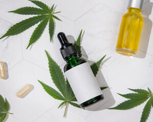 Dropper bottles with CBD oil and capsules near cannabis leaves top view, hard shadows