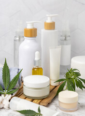 Obraz na płótnie Canvas Blank cosmetic jars, tubes and bottles near green cannabis leaves close up, CBD cosmetic mockup