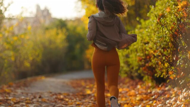 Hello autumn. Seen from behind middle aged woman in fitness clothes in the park running.