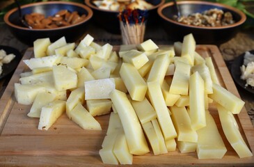 Appetizer of hard and soft cheese cut into strips and cubes on a wooden cutting board