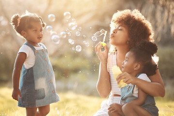 Nature, children and mother blowing bubbles in an outdoor park for playing, bonding or having fun....