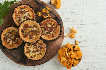 Savory hands pie with chanterelle mushrooms, cream and cheese on cutting board on rustic old white wooden table background. Homemade tarts with seasonal chanterelle mushrooms. Rustic style. Top view.