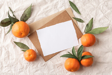 Natural winter stationery, desktop mock-up scene. Blank eco greeting card, craft envelope, with mandarins on beige linen tablecloth background. Flat lay, top view. Winter rustic composition