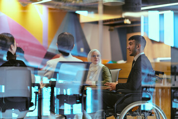 In a modern glass startup office, a wheelchair-bound director leads a successful meeting with...
