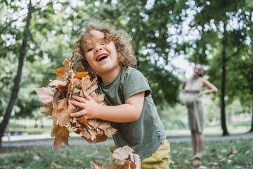 portrait of happy boy playing on the grass with dry leaves in a park on sunny day
