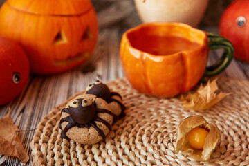 Aesthetic autumn Halloween cookies in shape of spider with cup of tea among pumpkins and fragrant leaves