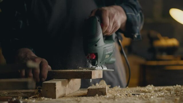 Industry, Caucasian male woodworker working with an electronic jigsaw cutting wood in a carpentry workshop Wood specialist Is in a dark atmospheric room At the workplace, carpentry workshop