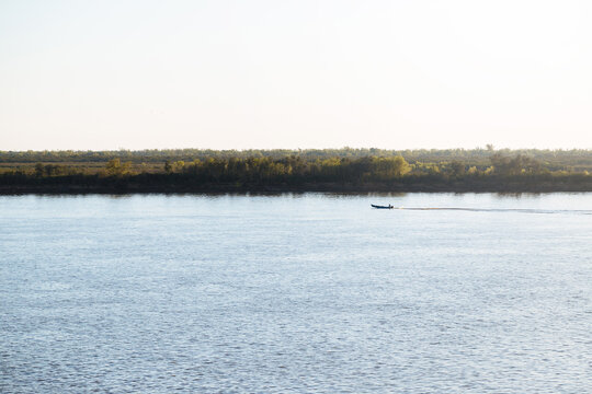 View of the Parana river in front of the city of Rosario. A fishing boat navigates it.Bright, clear morning sky and the forest at the water's edge.