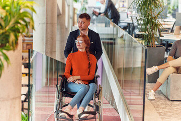 A company director assists his business colleague in a wheelchair, helping her navigate to their startup office, where they work alongside their diverse team of colleagues, emphasizing inclusivity and
