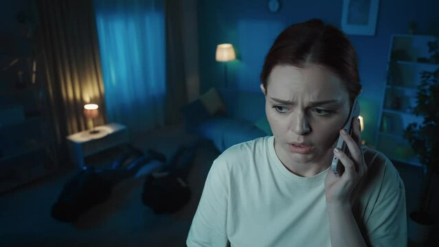 Video of a young woman standing on a foreground in a dark room with two tied up burglars, intruders lying on the floor. She calls emergency hotline for help.